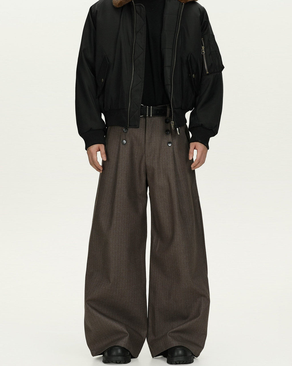 Person wearing a black jacket and brown wide-leg pants on a white background