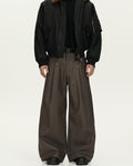 Person wearing a black jacket and brown wide-leg pants on a white background