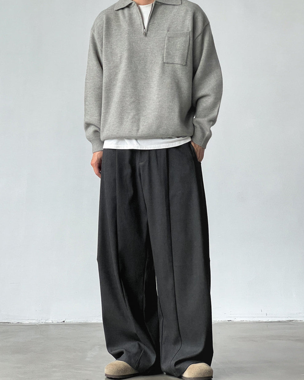 Person wearing a gray sweater and black wide-leg pants against a white background