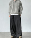 Person wearing a gray sweater and black wide-leg pants against a white background
